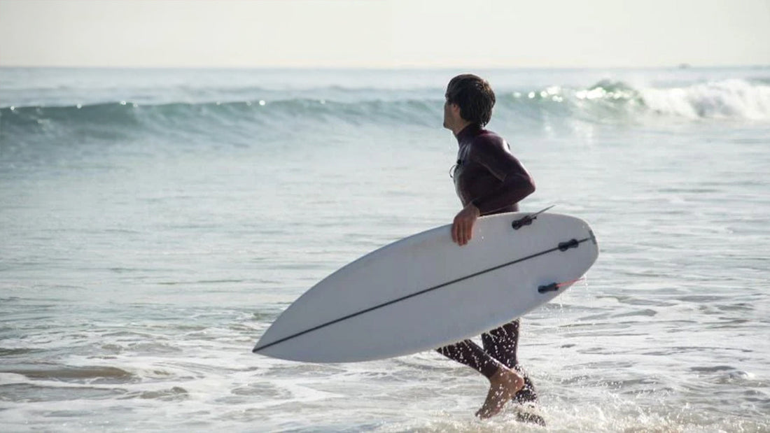 6 best wetsuits for spring with a man running into a sea holding a surfboard