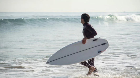6 best wetsuits for spring with a man running into a sea holding a surfboard