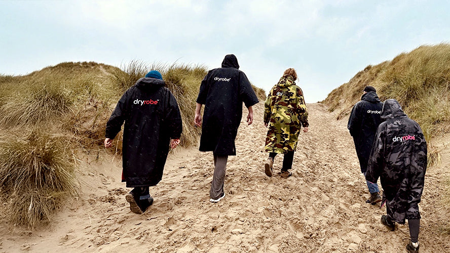 people walking over sand dunes at the beach wearing changing robes