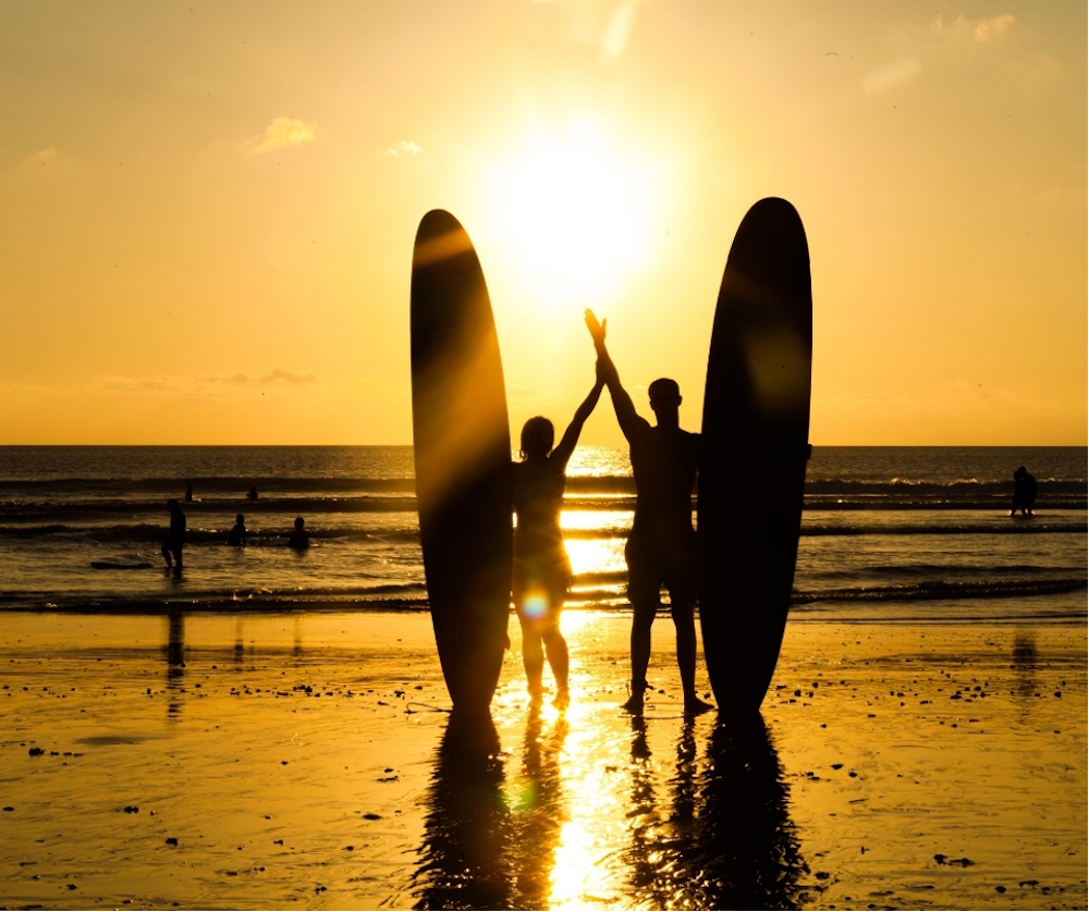 Two surfers holding their surfboards in the sunset