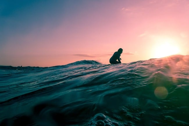 A surfer sat on a board against a sunset