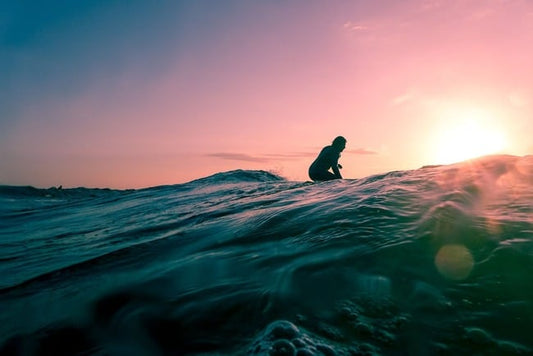 A surfer sat on a board against a sunset