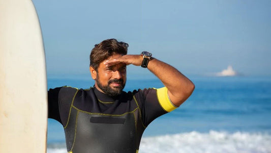 A man wearing a shorty wetsuit looking into the horizon holding up a surfboard