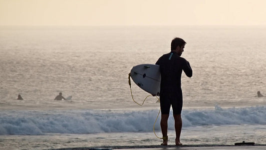 surfer wearing a wetsuit and holding a shortboard in front of breaking waves
