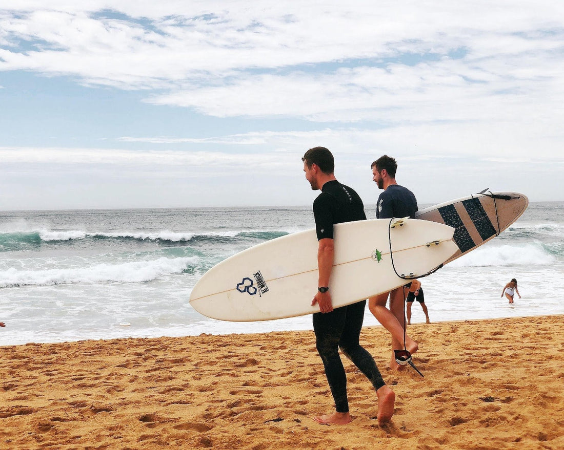 Two men carrying surfboards walking toward the water