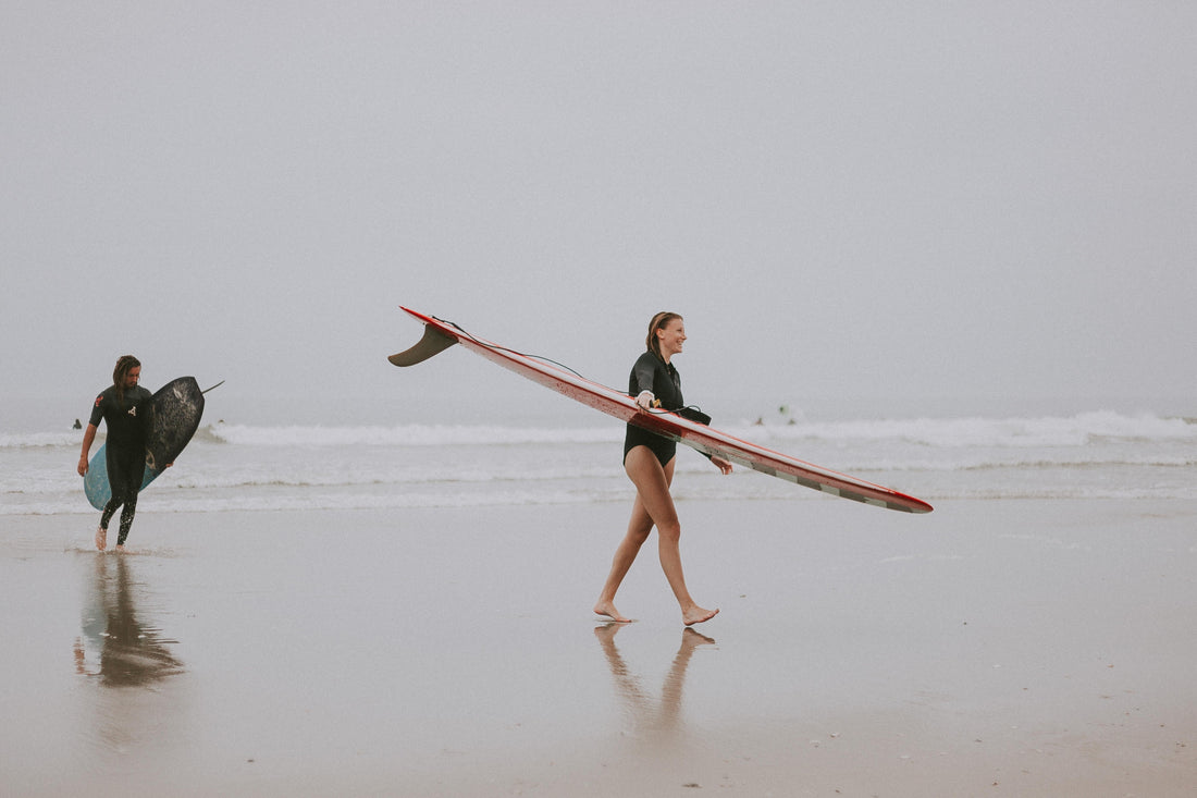 A woman and man carrying their surfboards across the beach