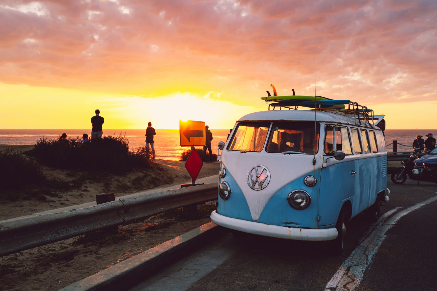 vw camper van with surfboards on roof next to beach at sunset