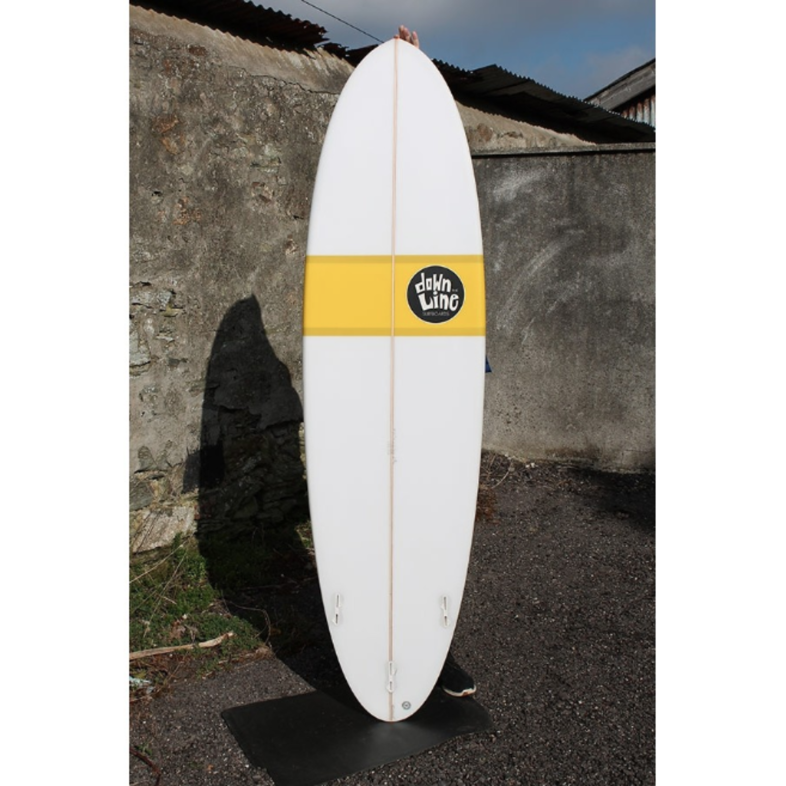 Fun surfboard in white with a yellow strip and black and white logo on a lifestyle shot background
